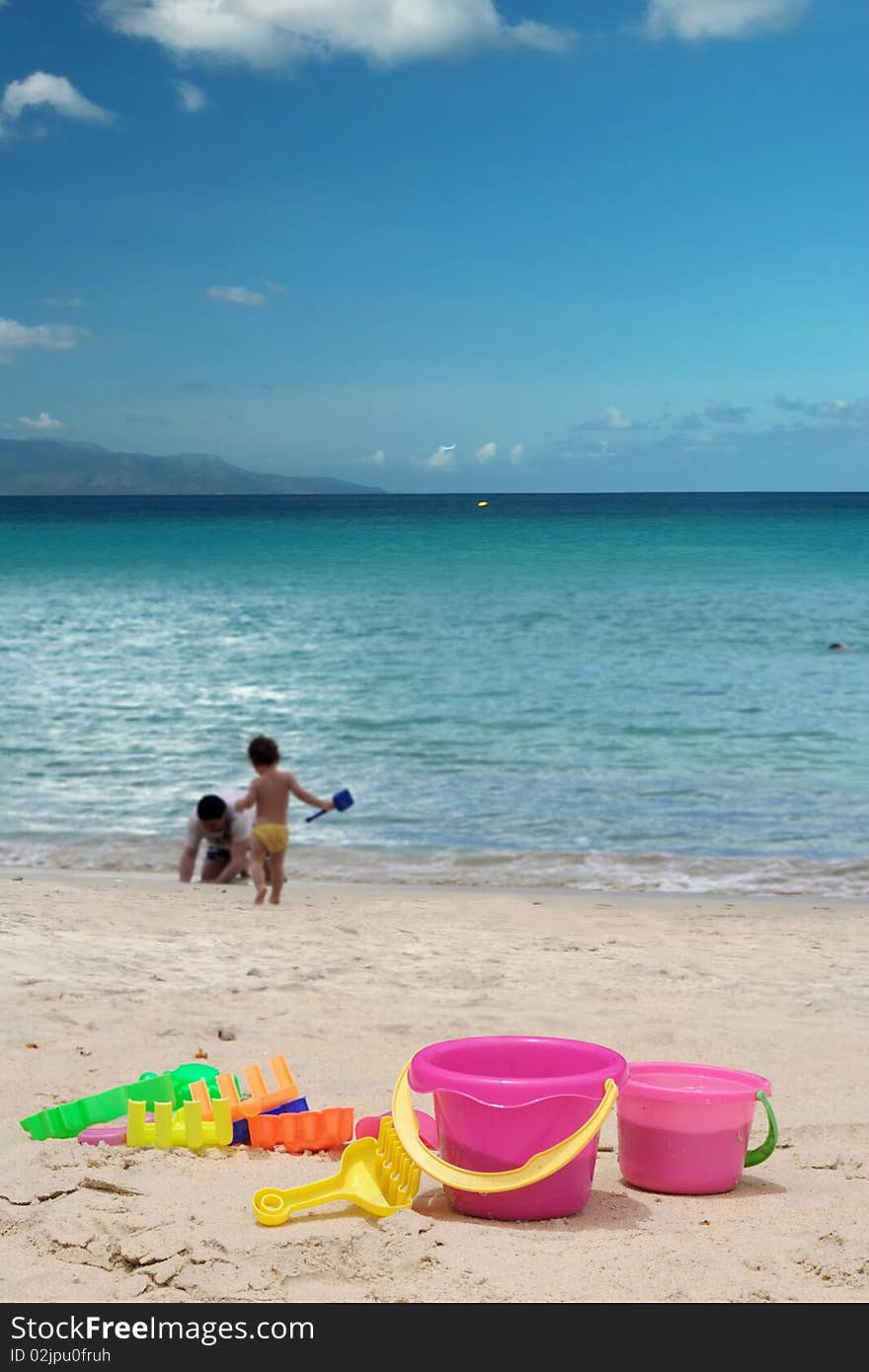 The children toys on beach . Motioned people (father and son) are plying on the beach. Tropical sea , sky, island on horizon as background. The area of sky is free for your text . The children toys on beach . Motioned people (father and son) are plying on the beach. Tropical sea , sky, island on horizon as background. The area of sky is free for your text .