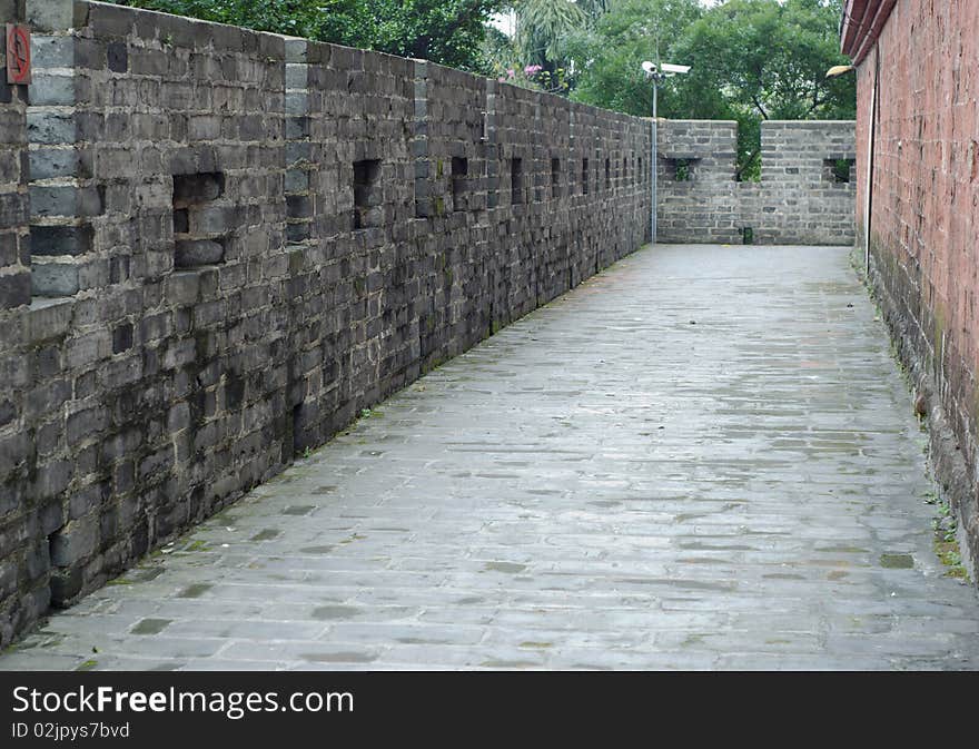 This shot is of stone side walk with walls on either side. The wall on the right is grey, the wall on the left is red. A set of security cameras can be seen in the back side of the image. This shot is of stone side walk with walls on either side. The wall on the right is grey, the wall on the left is red. A set of security cameras can be seen in the back side of the image.