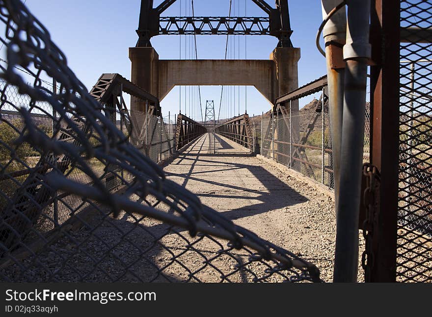 View through the fence of an old condemned suspension bridge in the desert. View through the fence of an old condemned suspension bridge in the desert