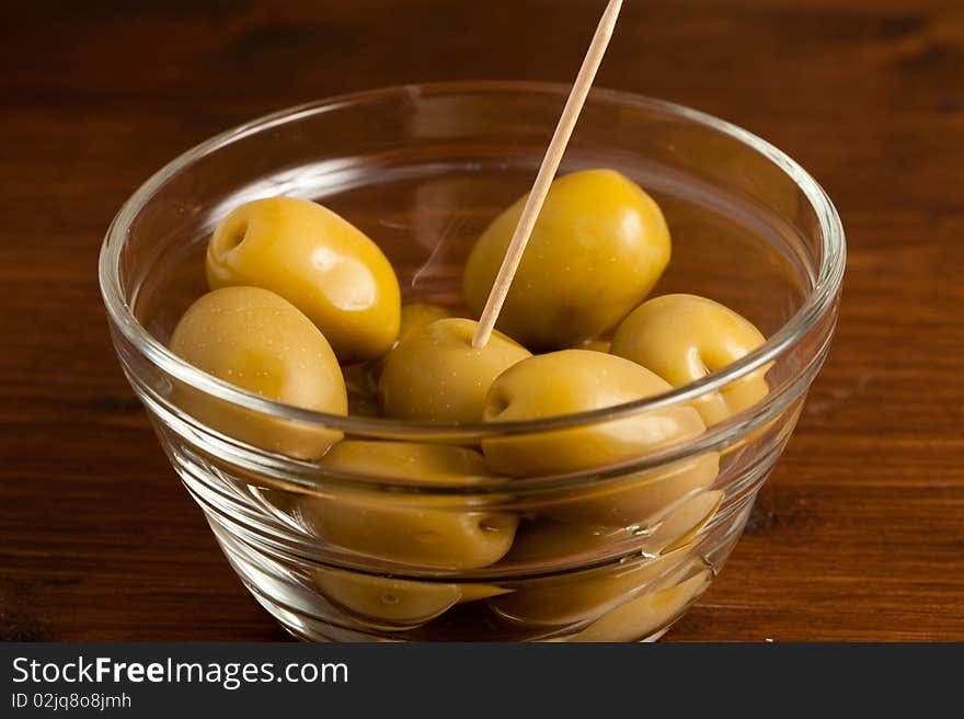 Photo of green olives in a bowl standing on a wood table