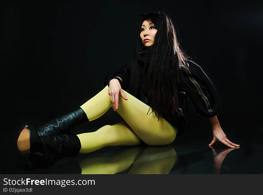 Sitting brunette asian model on black background with night reflections