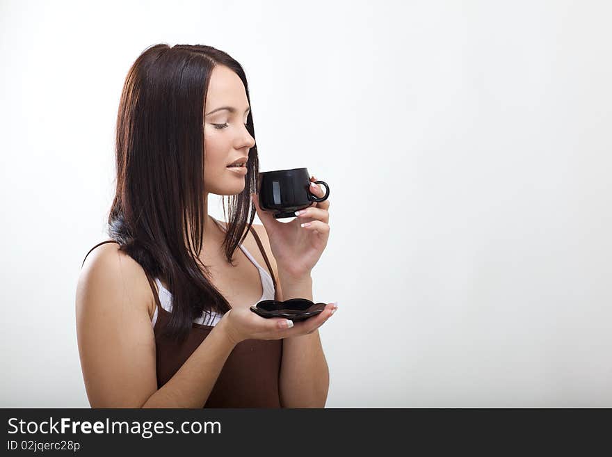 Beautiful young brunette drinking coffee in the studio with rear blym background