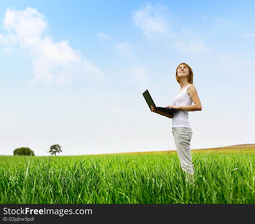 Young smiling woman with laptop standing on meadow with green grass