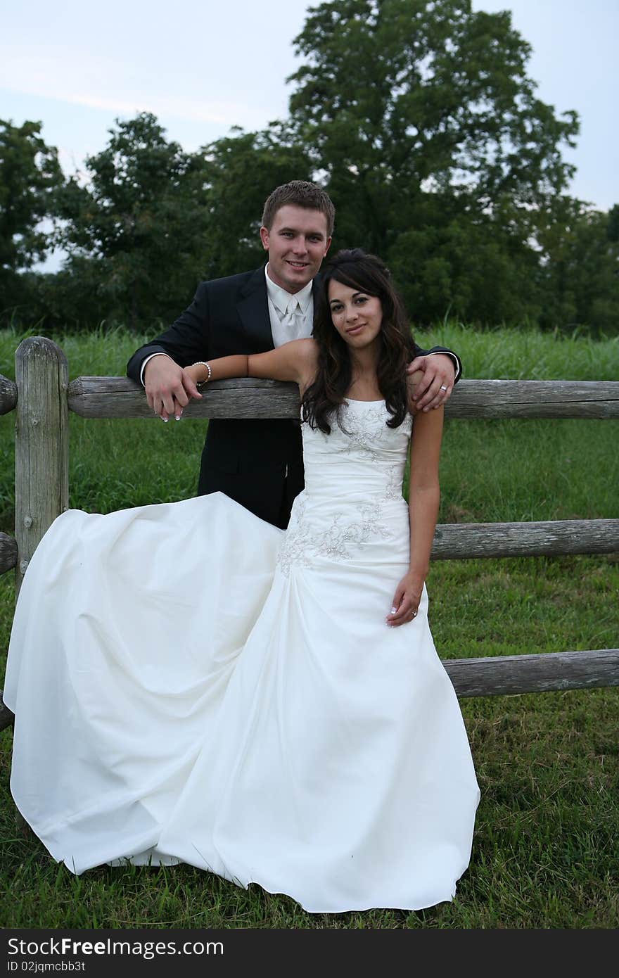 Attractive married couple standing together looking at  camera leaning against fence. Attractive married couple standing together looking at  camera leaning against fence