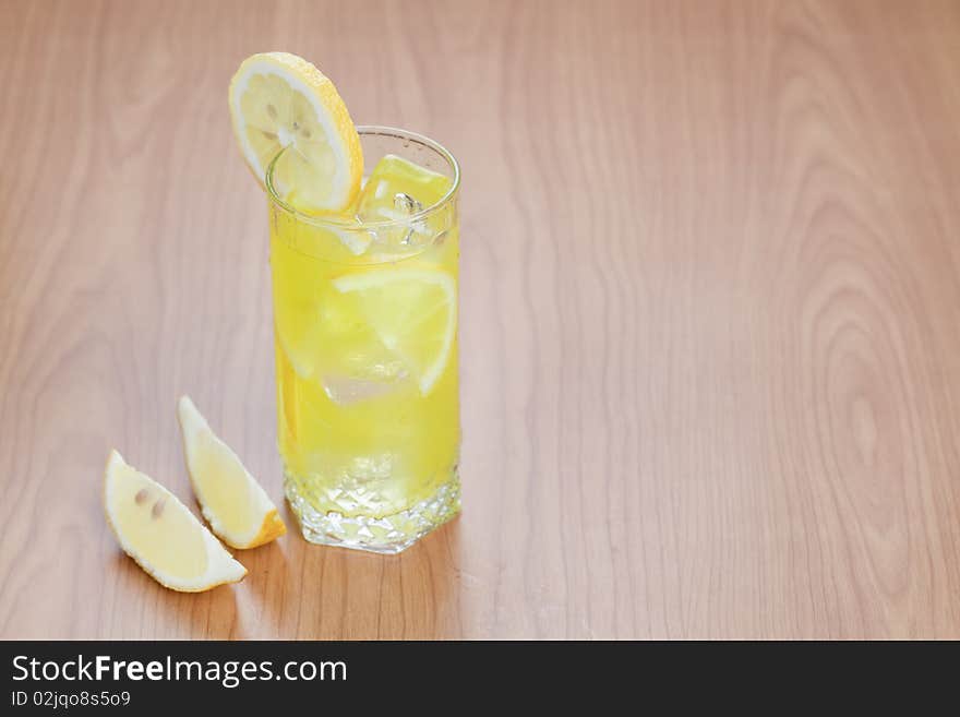 Glass of cold lemon beverage on wooden table top with space for text