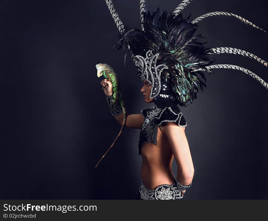 Young pagan priest in ritual suit with green iguana in his hands. Photo.