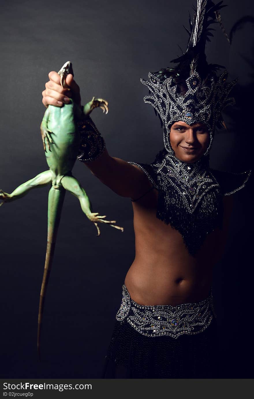 Young pagan priest in ritual suit with green iguana in his hands. Photo.