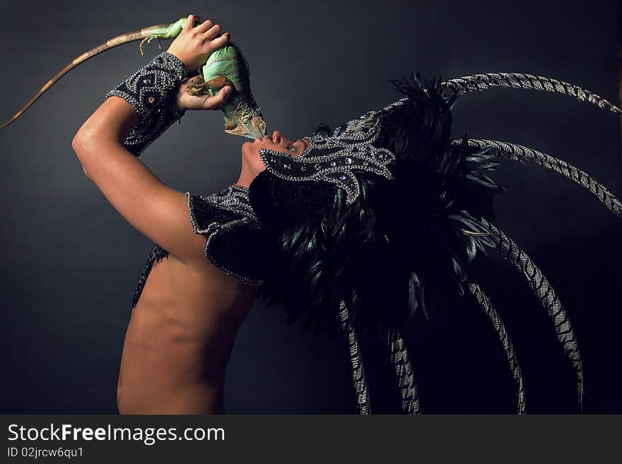 Young pagan priest in ritual suit with green iguana in his hands. Photo.