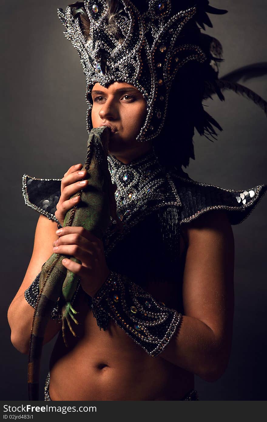 Young pagan priest in ritual suit with green iguana in his hands. Photo.