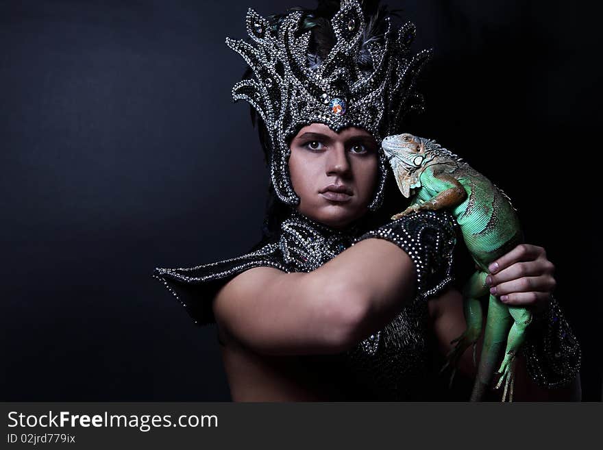 Young pagan priest in ritual suit with green iguana in his hands. Photo.