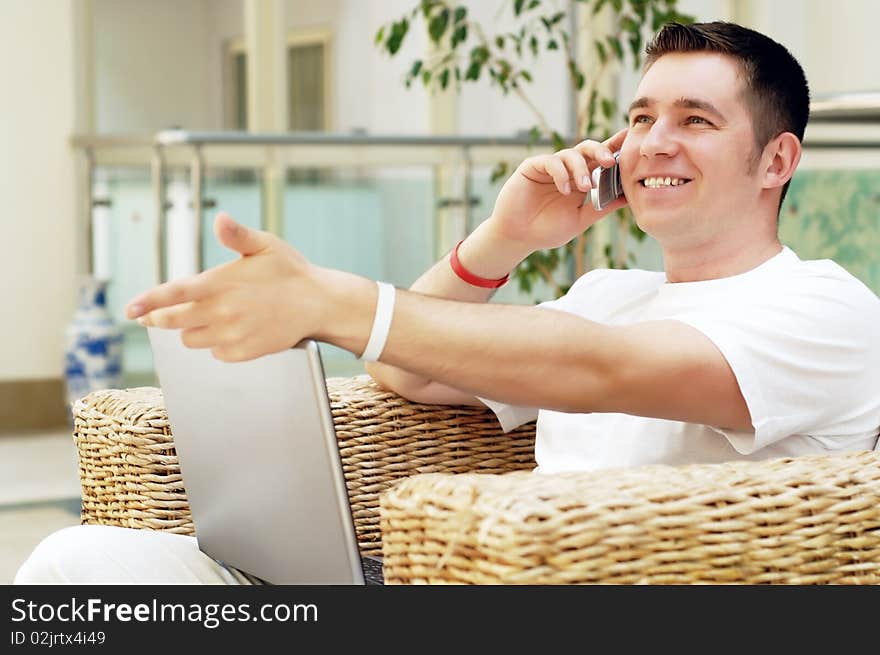 Smiling young man working on laptop computer and call by phone at home