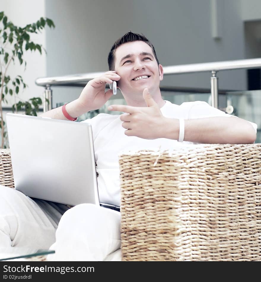 Smiling young man working on laptop computer and call by phone at home