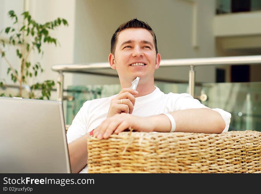 Smiling young man working on laptop computer and call by phone at home