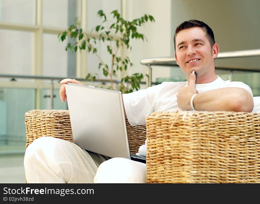 Smiling young man working on laptop computer and call by phone at home