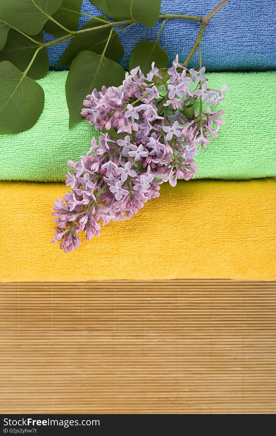 Colored towels folded lie next to them a branch of lilac. Colored towels folded lie next to them a branch of lilac