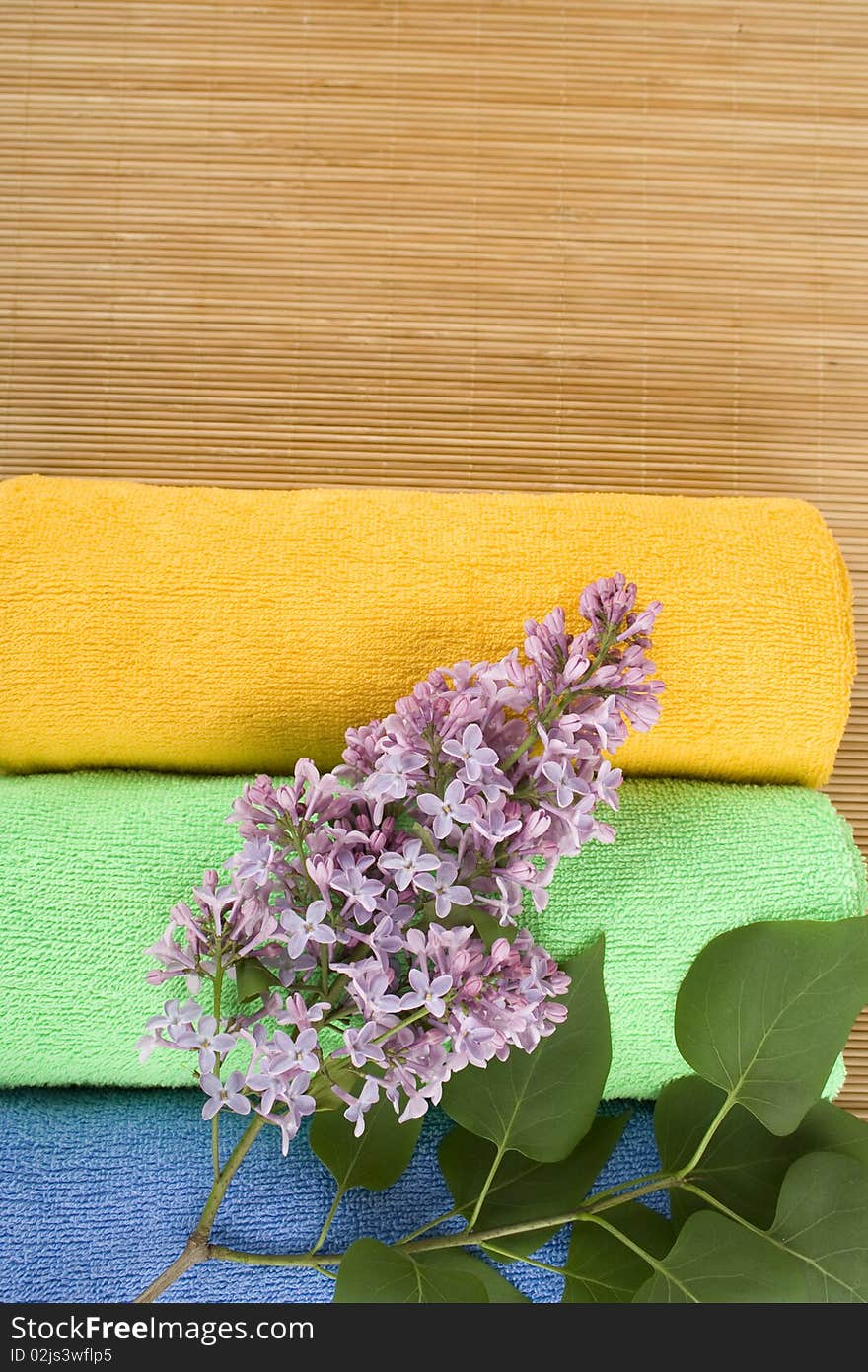 Colored towels folded lie next to them a branch of lilac. Colored towels folded lie next to them a branch of lilac