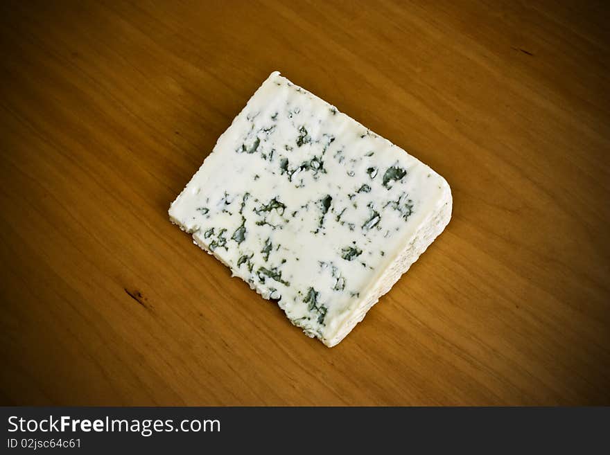 A slice of creamy blue cheese on a wooden board. A slice of creamy blue cheese on a wooden board