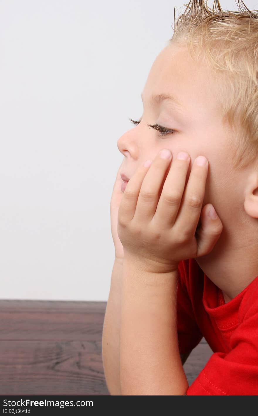 Portrait of a blond boy wearing a red shirt, face in his palms. Portrait of a blond boy wearing a red shirt, face in his palms