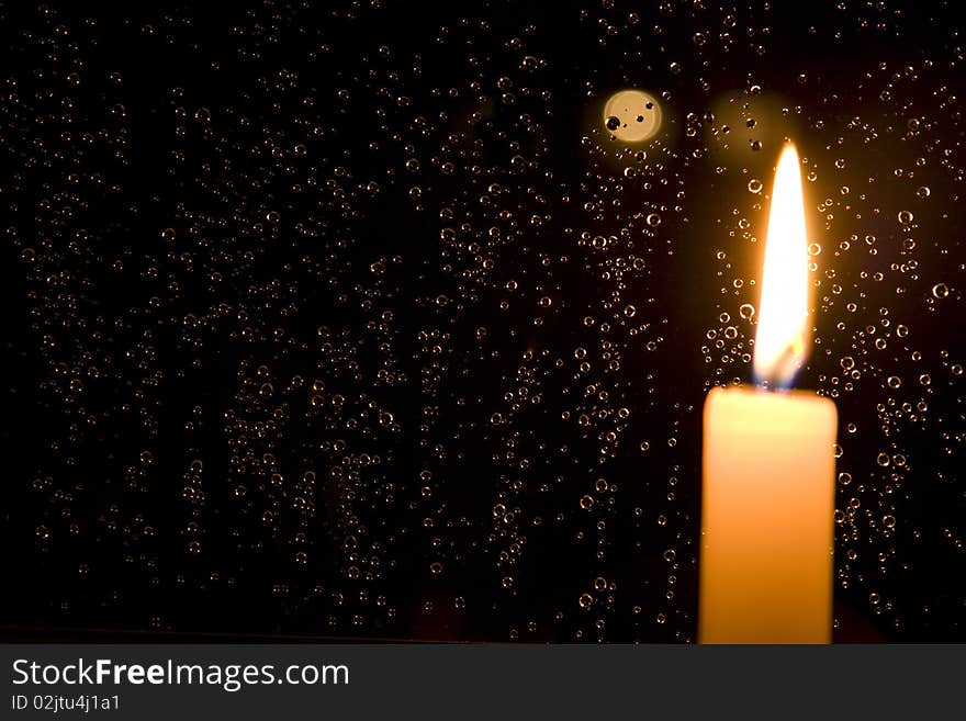 Rain drops reflect light of a burning candle in glass at night. Rain drops reflect light of a burning candle in glass at night