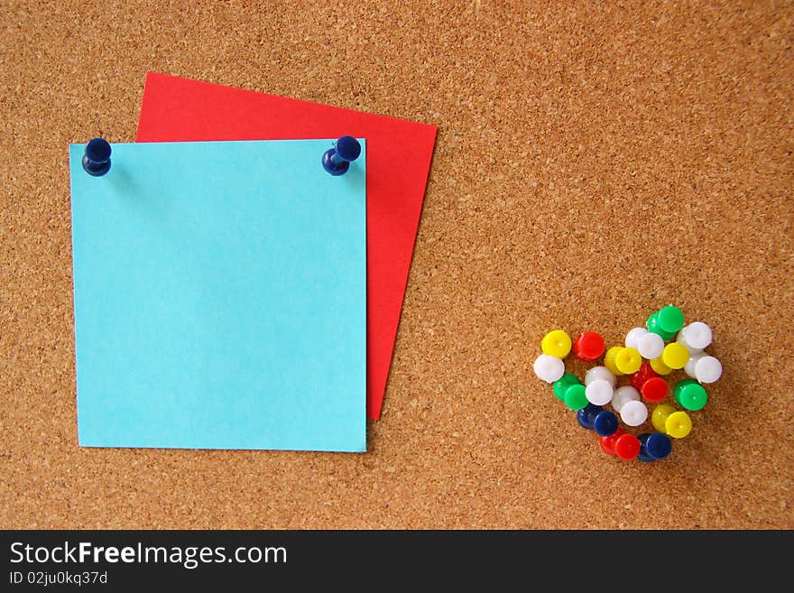 Red and blue post-it notes with many pushpins in a shape of a heart on corkboard