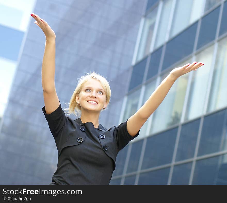 A young and attractive business woman is holding her hands up as a sign of success. Image taken outdoors, on a modern background.