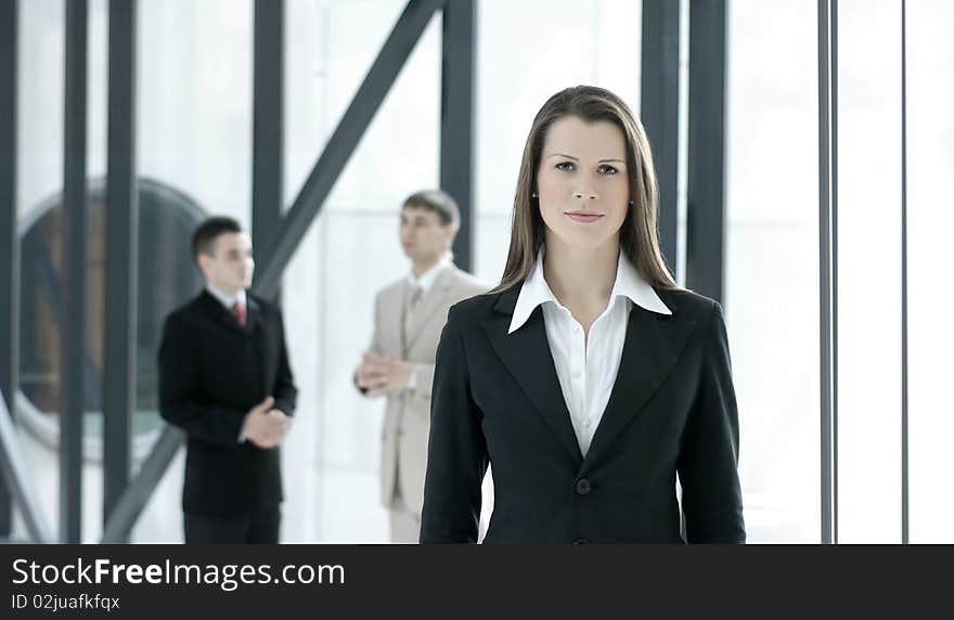 A young and attractive business woman is standing in front of her male colleagues. Image taken in a modern office. A young and attractive business woman is standing in front of her male colleagues. Image taken in a modern office.