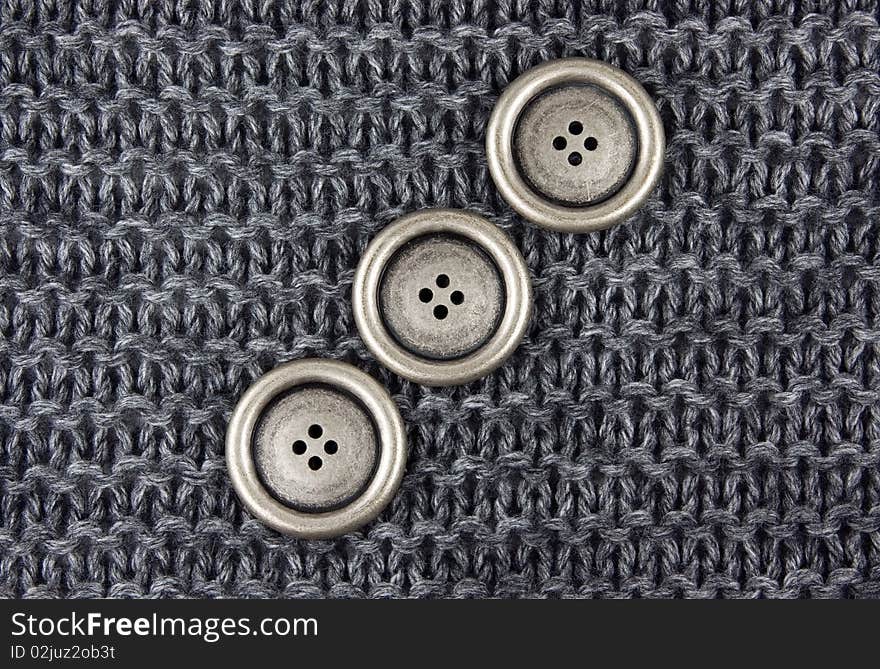 Three metal buttons on a gray knitted fabric background. Three metal buttons on a gray knitted fabric background