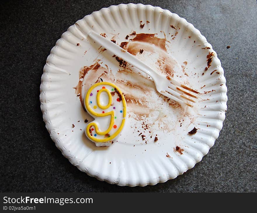 All that remains of a chocolaty ninth birthday cake and confetti-theme candle on a paper plate with a plastic fork. Nikon D40. All that remains of a chocolaty ninth birthday cake and confetti-theme candle on a paper plate with a plastic fork. Nikon D40.