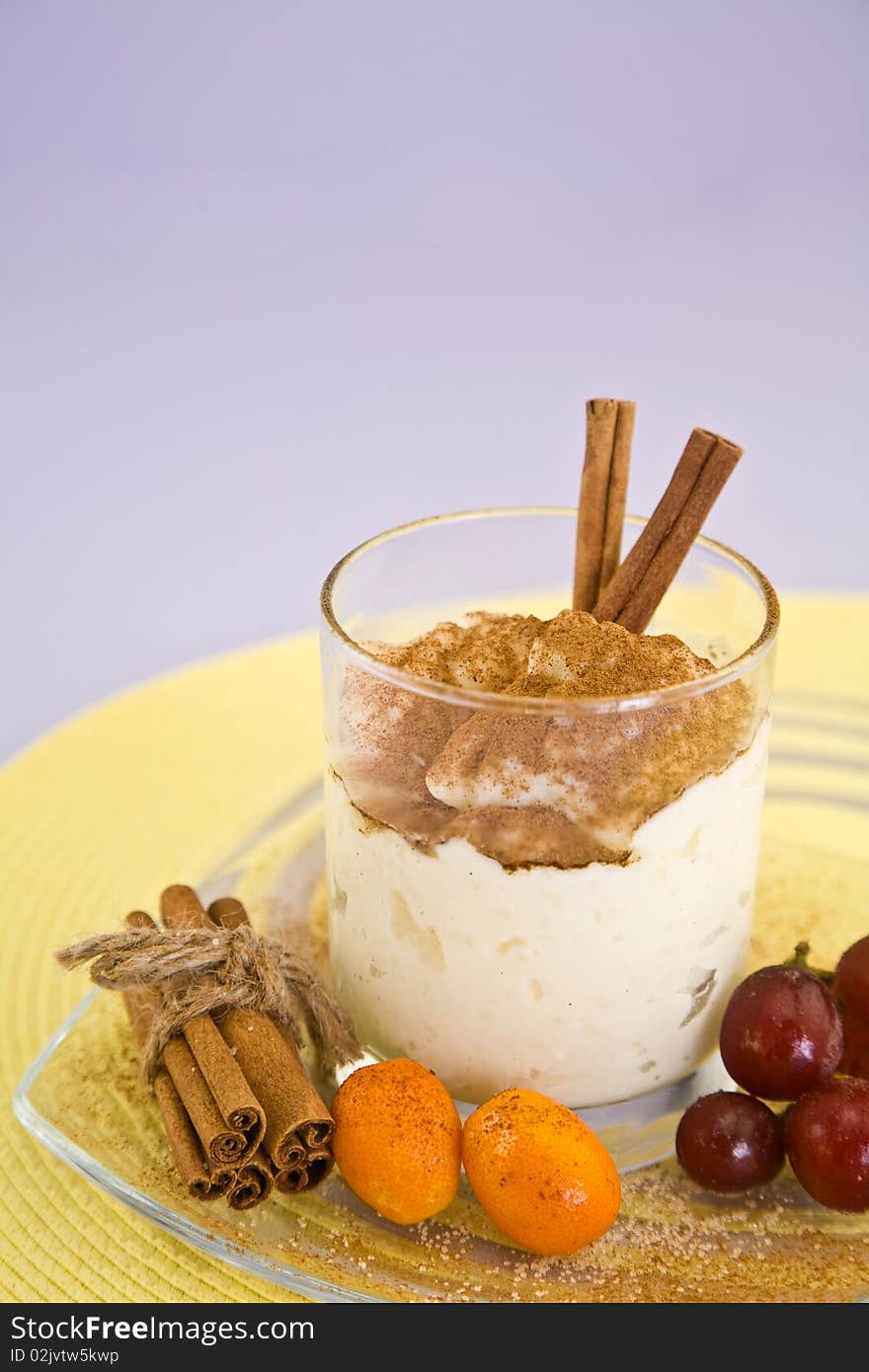 Rice pudding covered in cinnamon in glass. Rice dessert is surrounded by cinnamon sticks, cumquats and cherries. Rice pudding covered in cinnamon in glass. Rice dessert is surrounded by cinnamon sticks, cumquats and cherries.