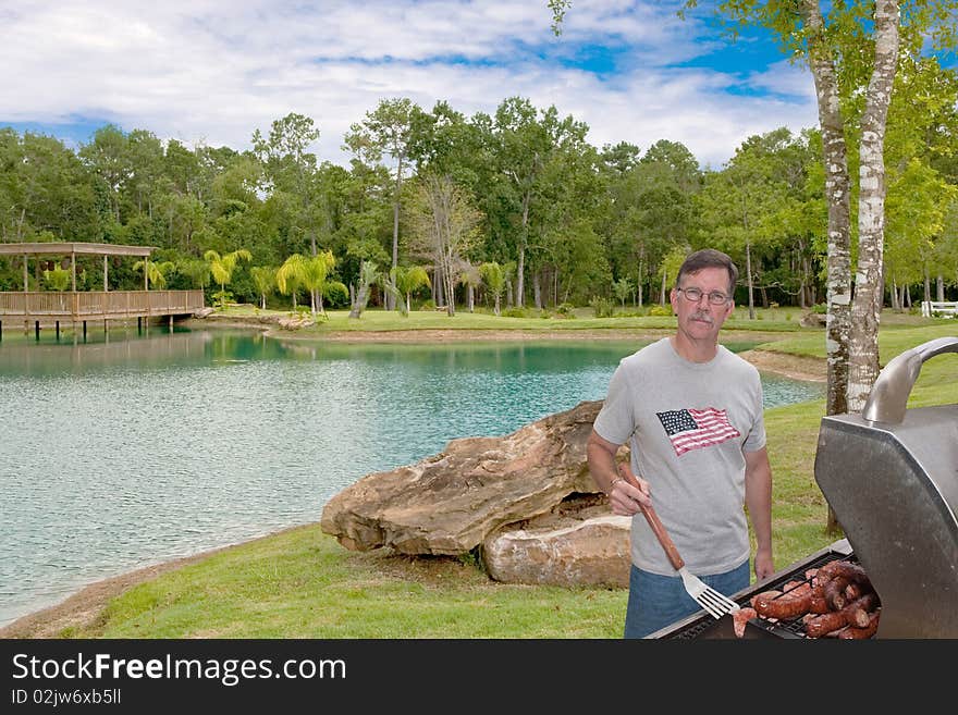 Mature young man in Park barbecuing hamburgers and sausages on a gas grill. Could be July 4th or other holiday. Mature young man in Park barbecuing hamburgers and sausages on a gas grill. Could be July 4th or other holiday.