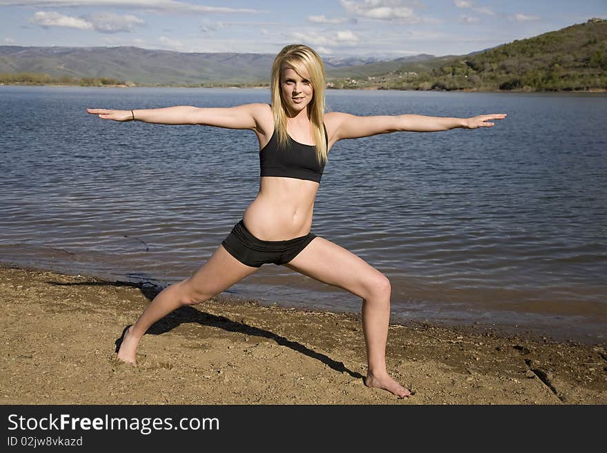 A woman on the beach by the water stretching out her body with a smile on her face. A woman on the beach by the water stretching out her body with a smile on her face.