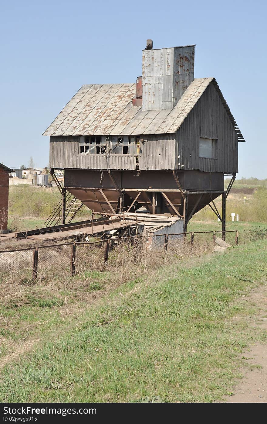 Barn for grain, old mill and grain elevator is at the village road, against a background of blue sky, made of wood and metal. Barn for grain, old mill and grain elevator is at the village road, against a background of blue sky, made of wood and metal