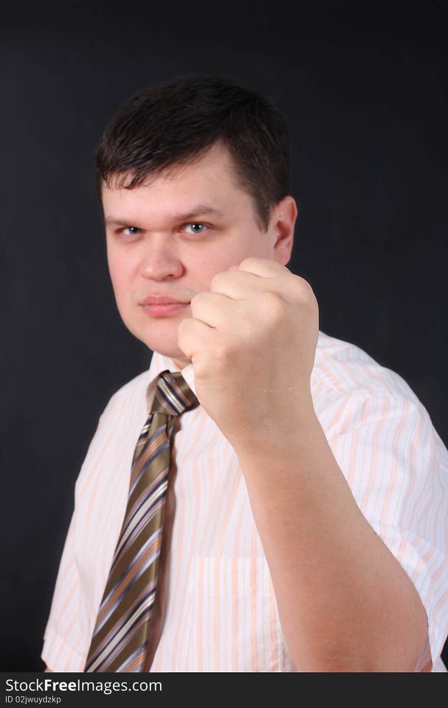 Serious the man shows a fist on a black background