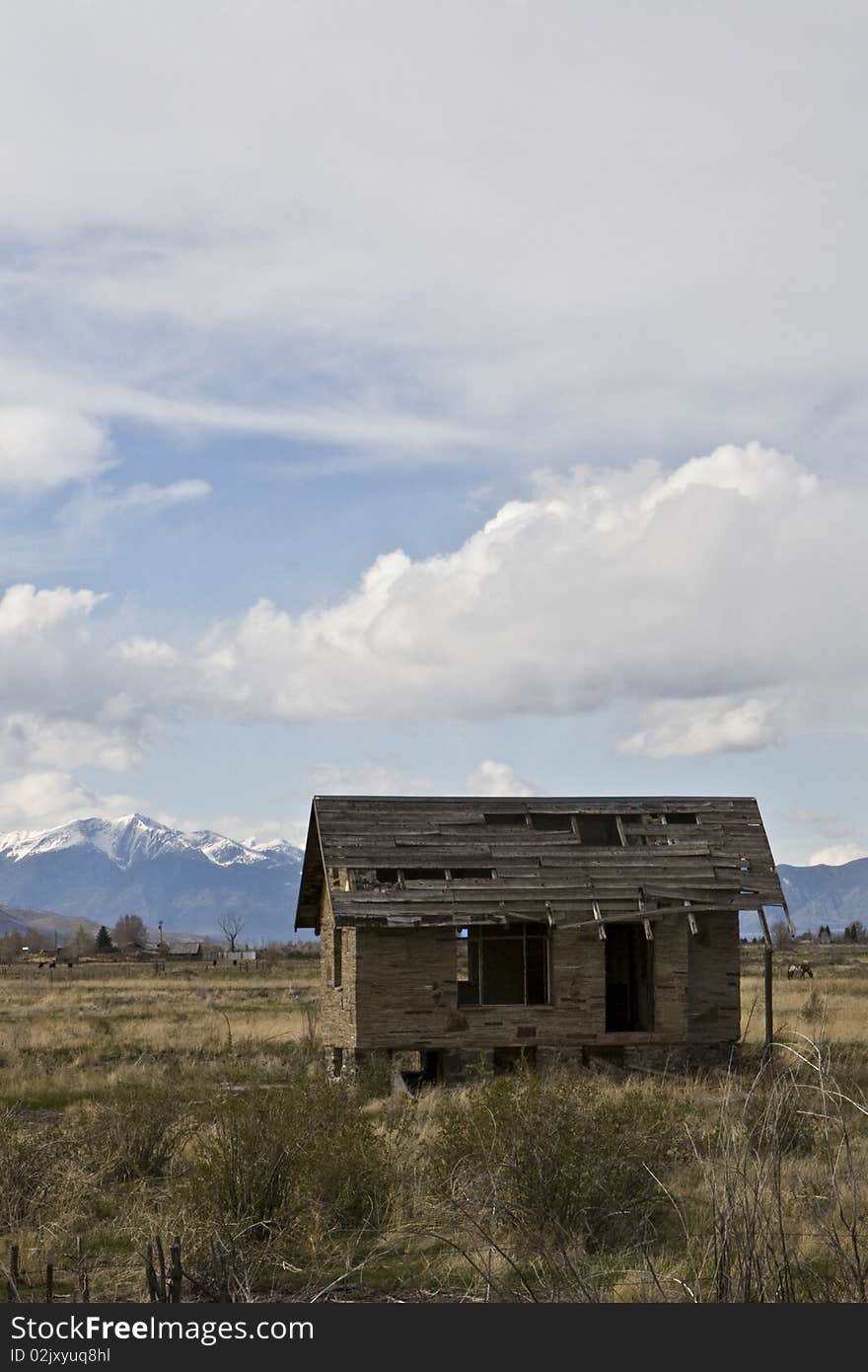 Abandoned one room plains house fallen into disrepair in Idaho with the snowcapped Targhee National Forest in the horizon