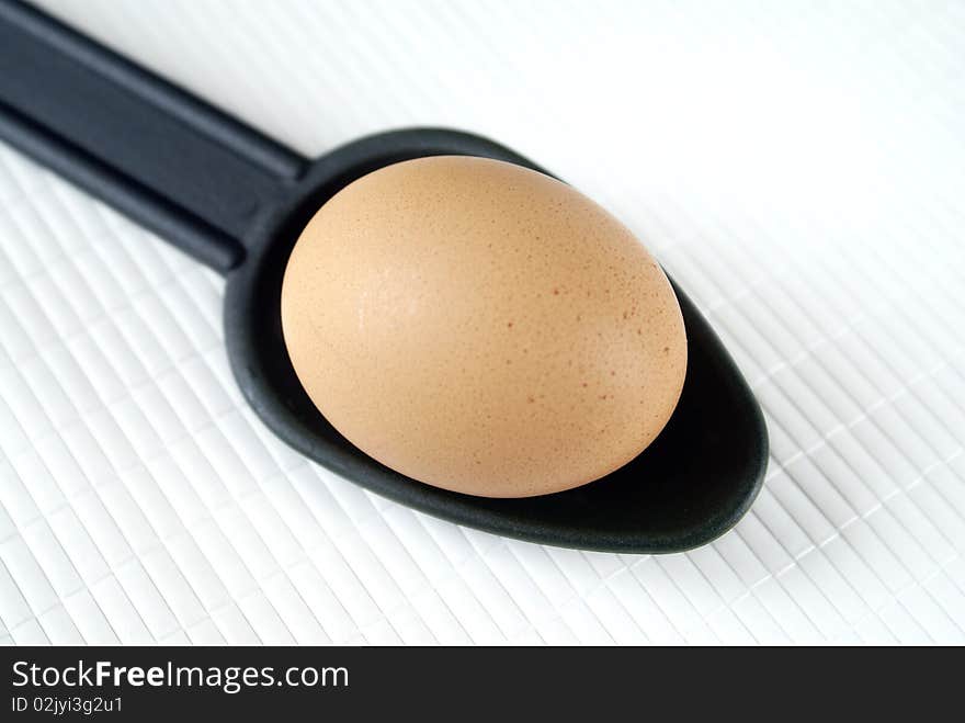 Raw egg on a white background and a spoon.