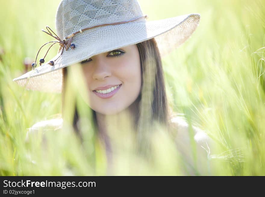 Young beautiful girl with hat staring at camera among green wheat. Young beautiful girl with hat staring at camera among green wheat.