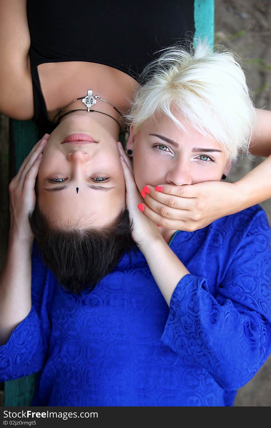 Conceptual photo: a girl closes the other girl ears, the second girl closes the other girl mouth. Conceptual photo: a girl closes the other girl ears, the second girl closes the other girl mouth