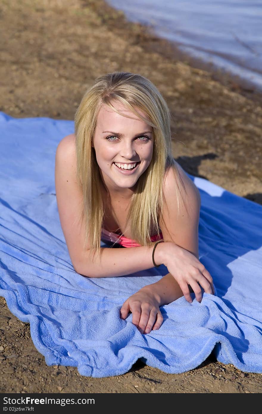 A woman laying and smiling while she is on a blue blanket on the beach. A woman laying and smiling while she is on a blue blanket on the beach.