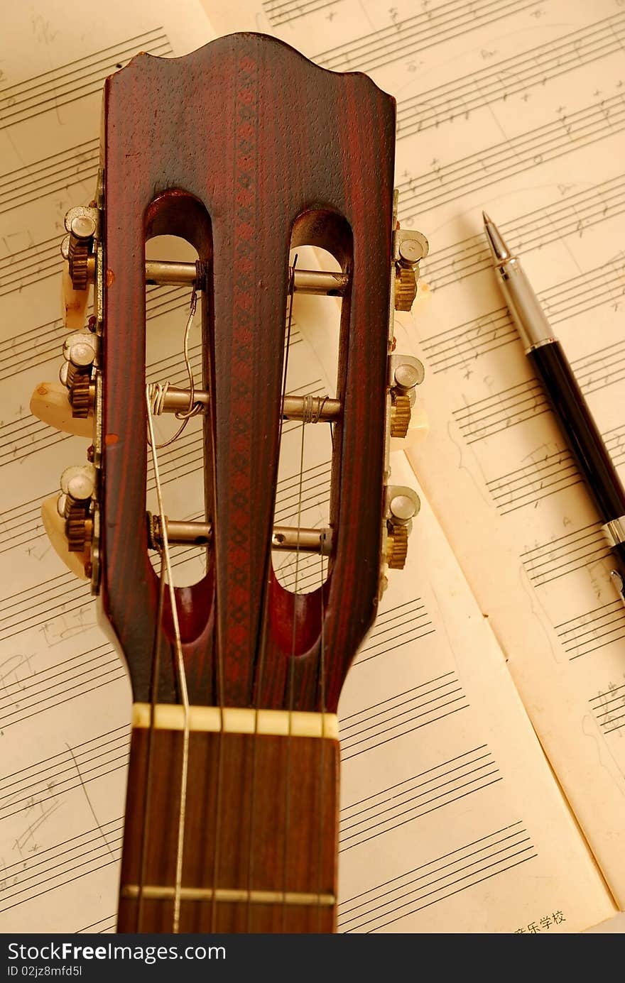 Guitar with pen on music manuscript with sepia effect. For concepts like music composition and creativity.