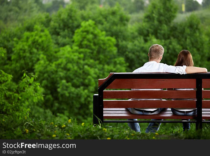 The enamoured couple sits on a bench against green trees