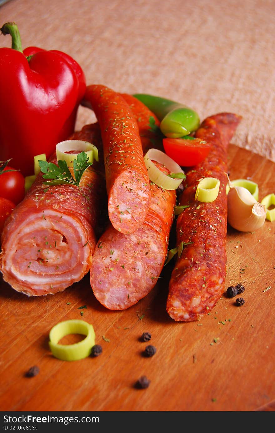 Various sausages on wooden plate with vegetables