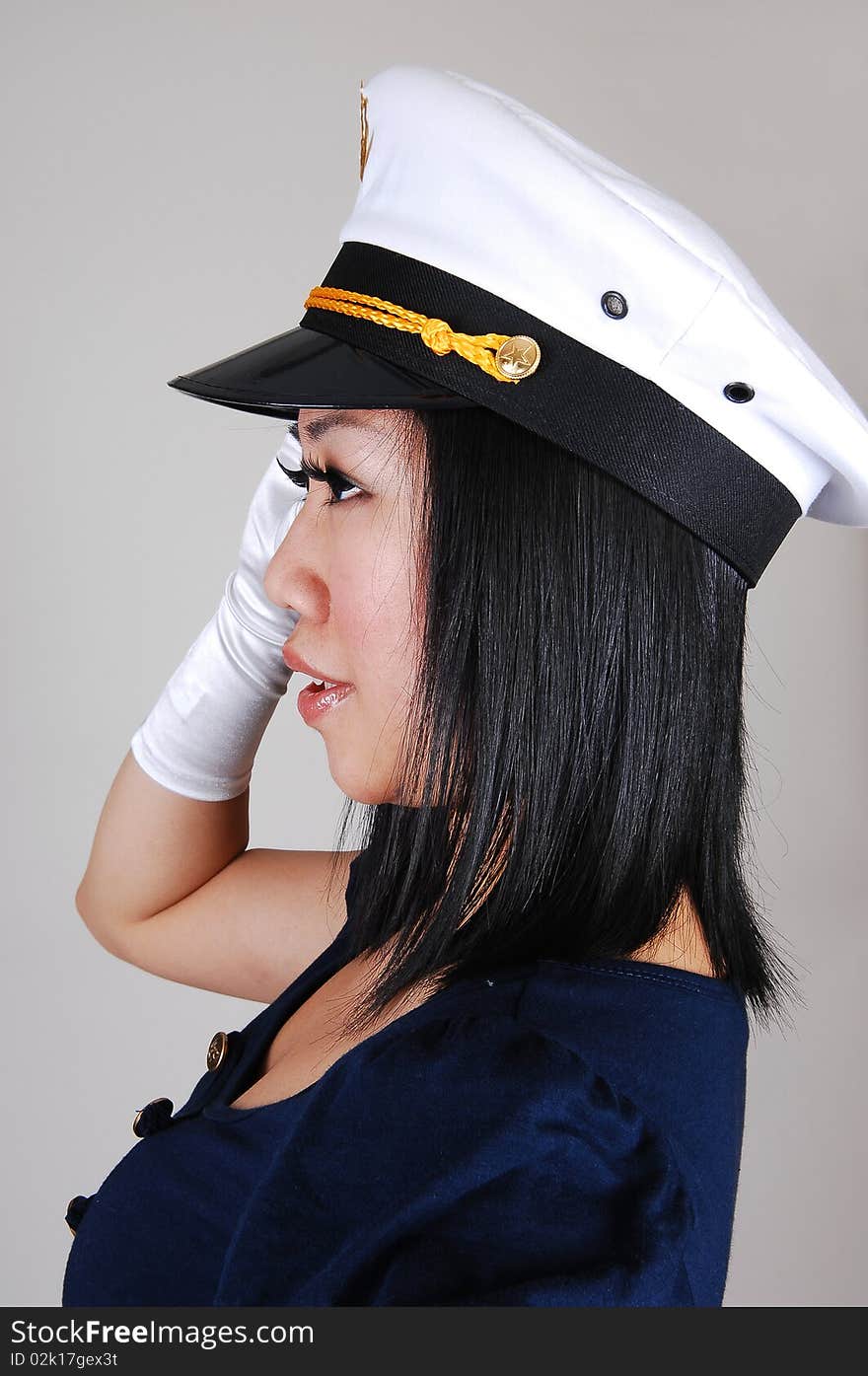 A young pretty Asian woman, in a sailor uniform and white gloves and sailor a cap , in an portrait, standing saluting in the studio for light gray background. A young pretty Asian woman, in a sailor uniform and white gloves and sailor a cap , in an portrait, standing saluting in the studio for light gray background.