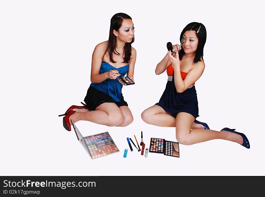 Two Asian woman sitting on the floor in the studio and helping each other with the makeup for the next photo shoot, for light gray background. Two Asian woman sitting on the floor in the studio and helping each other with the makeup for the next photo shoot, for light gray background.