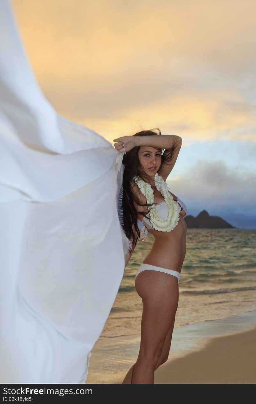 Beautiful young woman on lanikai beach at sunrise in a bikini with a long chiffon scarf