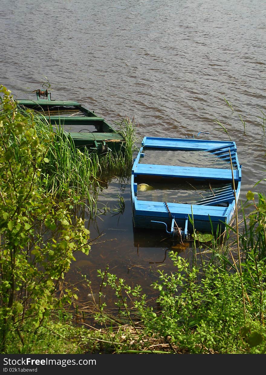 Two old fishing boat full of water at the edge of the pond