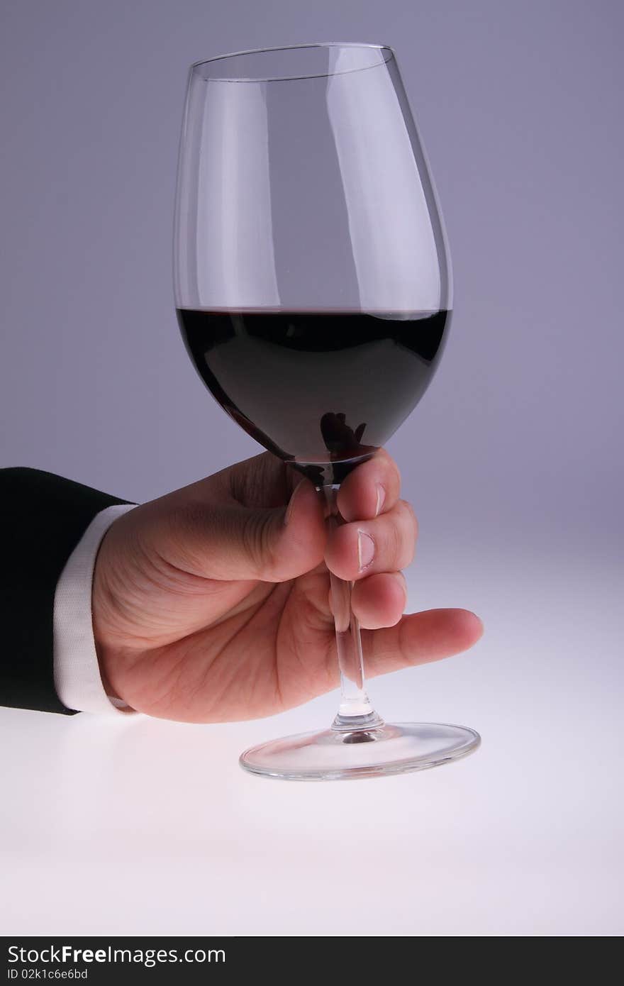 Image of glass of red wine held by a gentleman wearing a suit. Image of glass of red wine held by a gentleman wearing a suit.