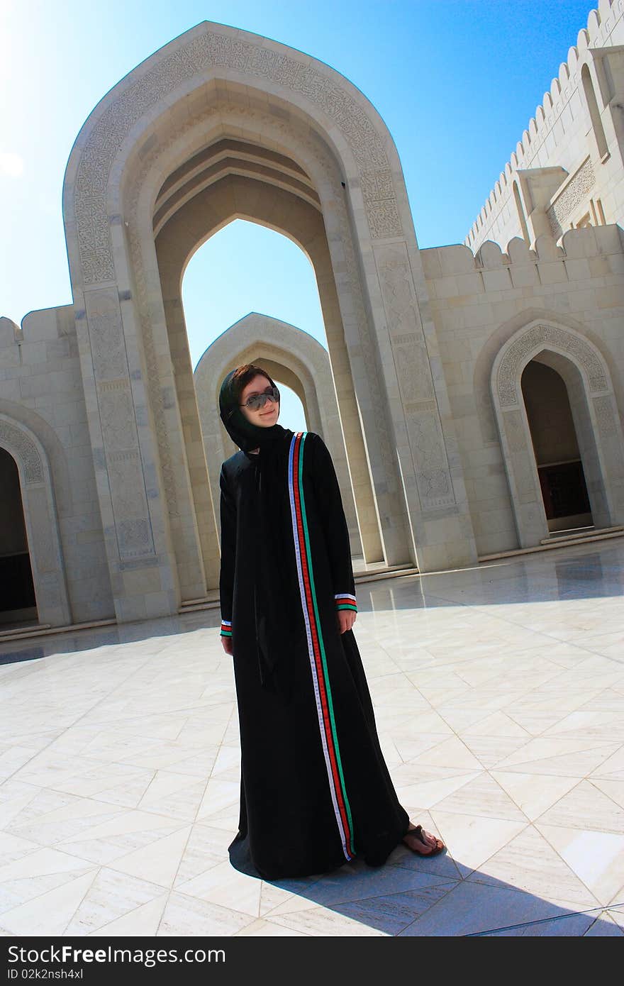 Young woman dressed up in traditional long black omani dress standing in the yard of a mosque. Young woman dressed up in traditional long black omani dress standing in the yard of a mosque