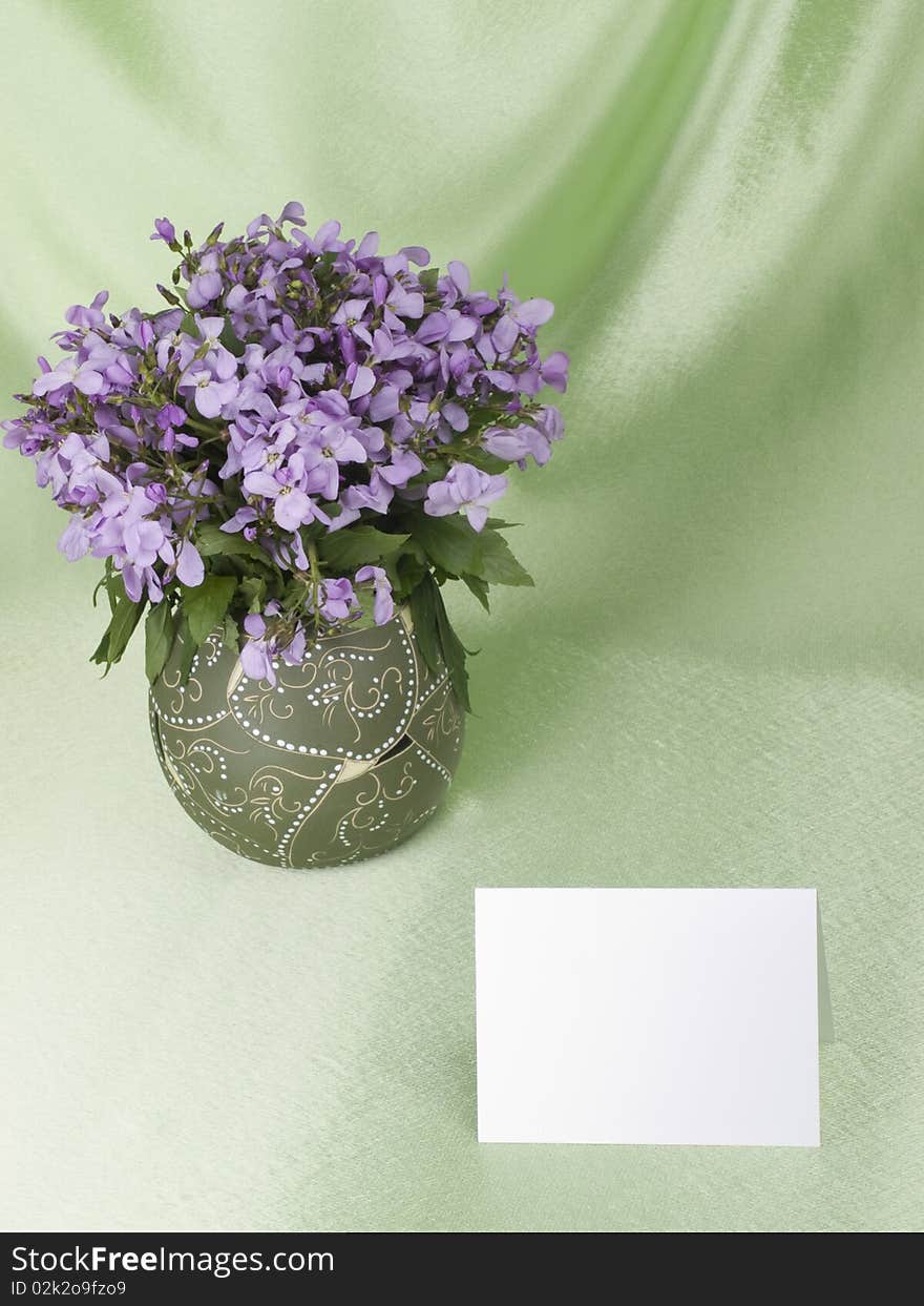 Flowers are in a vase and empty memo card with space for your own text, over green background