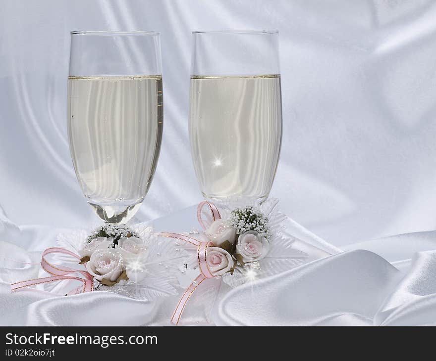 Two glasses with champagne and wedding decoration on white silk