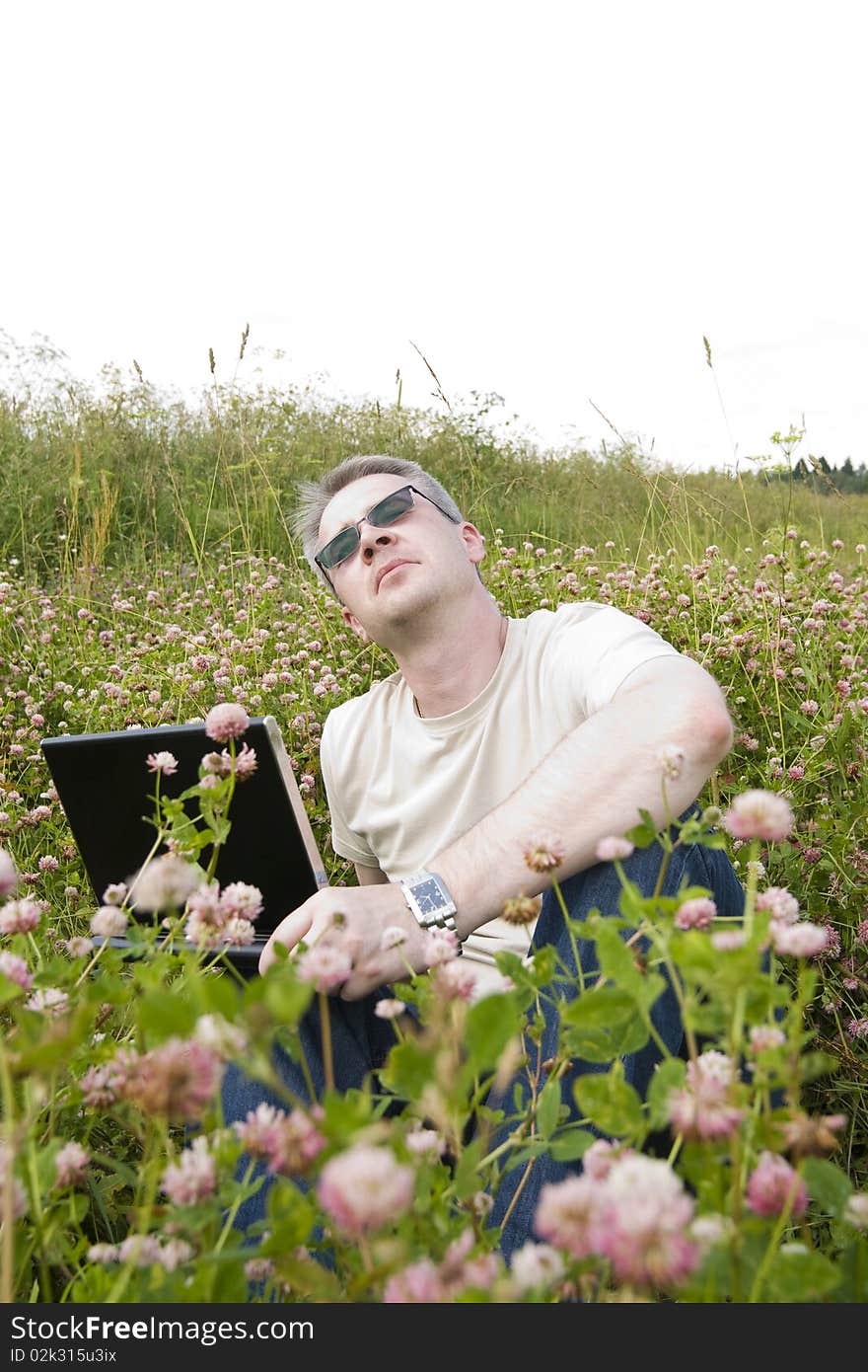 Thoughtful man with laptop on meadow